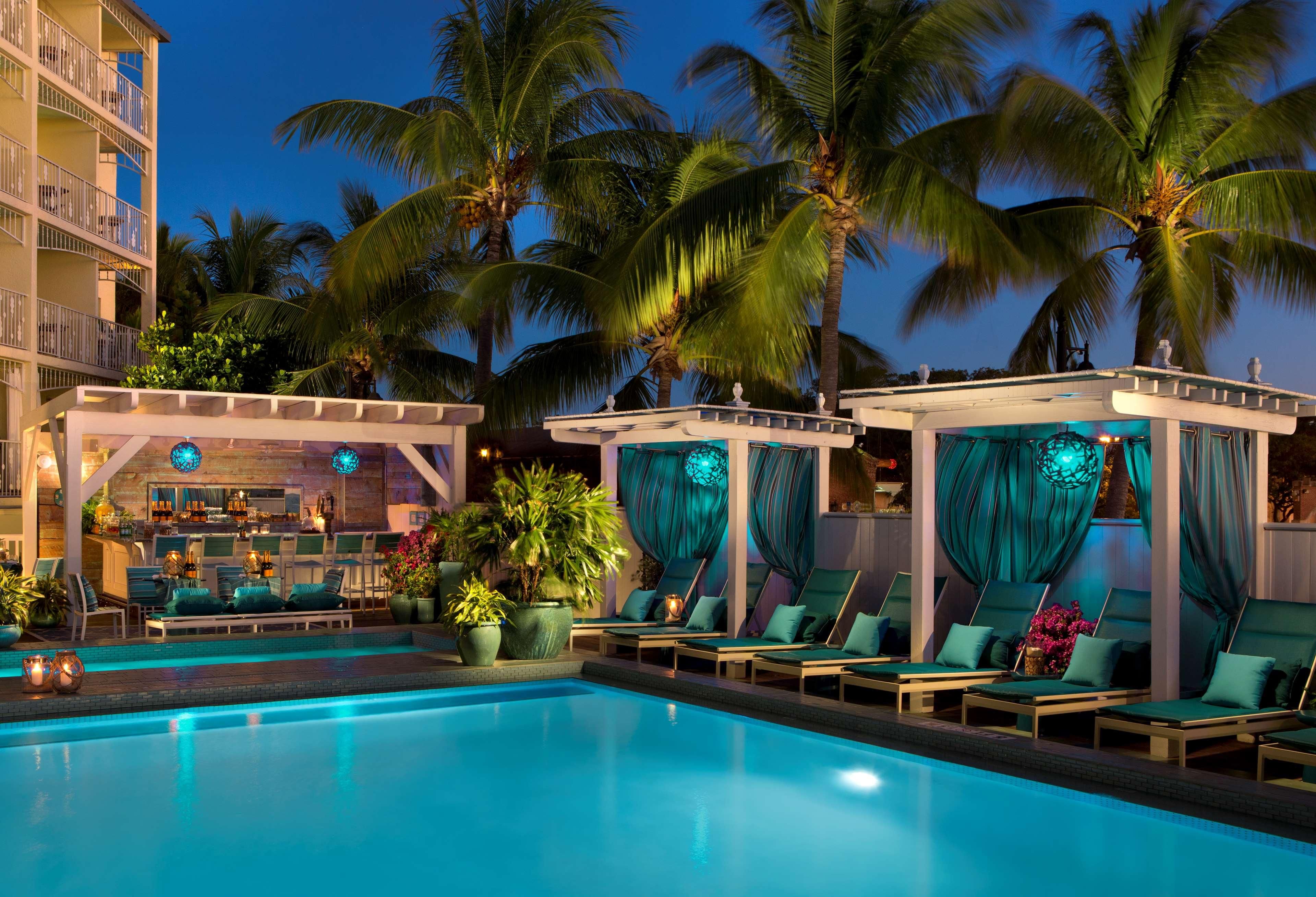 A pool area with lounge chairs and a bar, surrounded by palm trees.