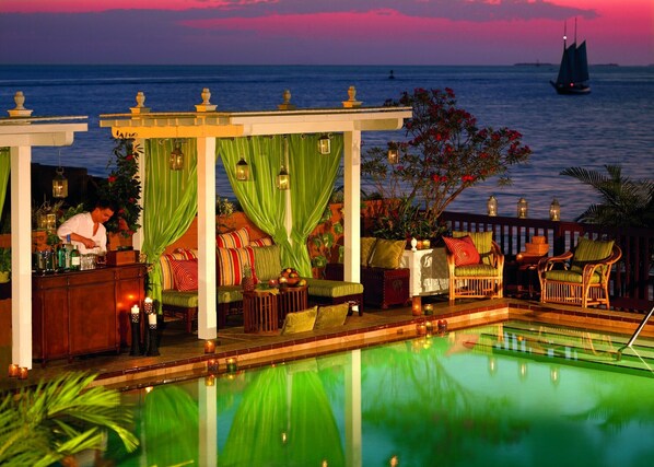 A poolside bar with seating and a view of the ocean at dusk.