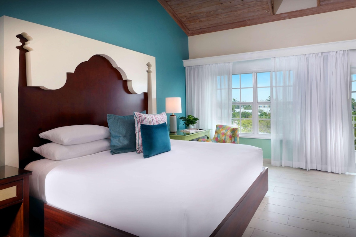A bedroom with a large bed, a wooden headboard, a nightstand, a lamp, and a window with curtains.