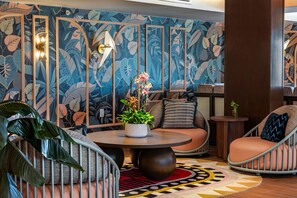 Ein stilvoller Lounge-Bereich mit rundem Tisch, gepolsterten Sitzmöglichkeiten und einer Wand mit tropischem Blattmuster.