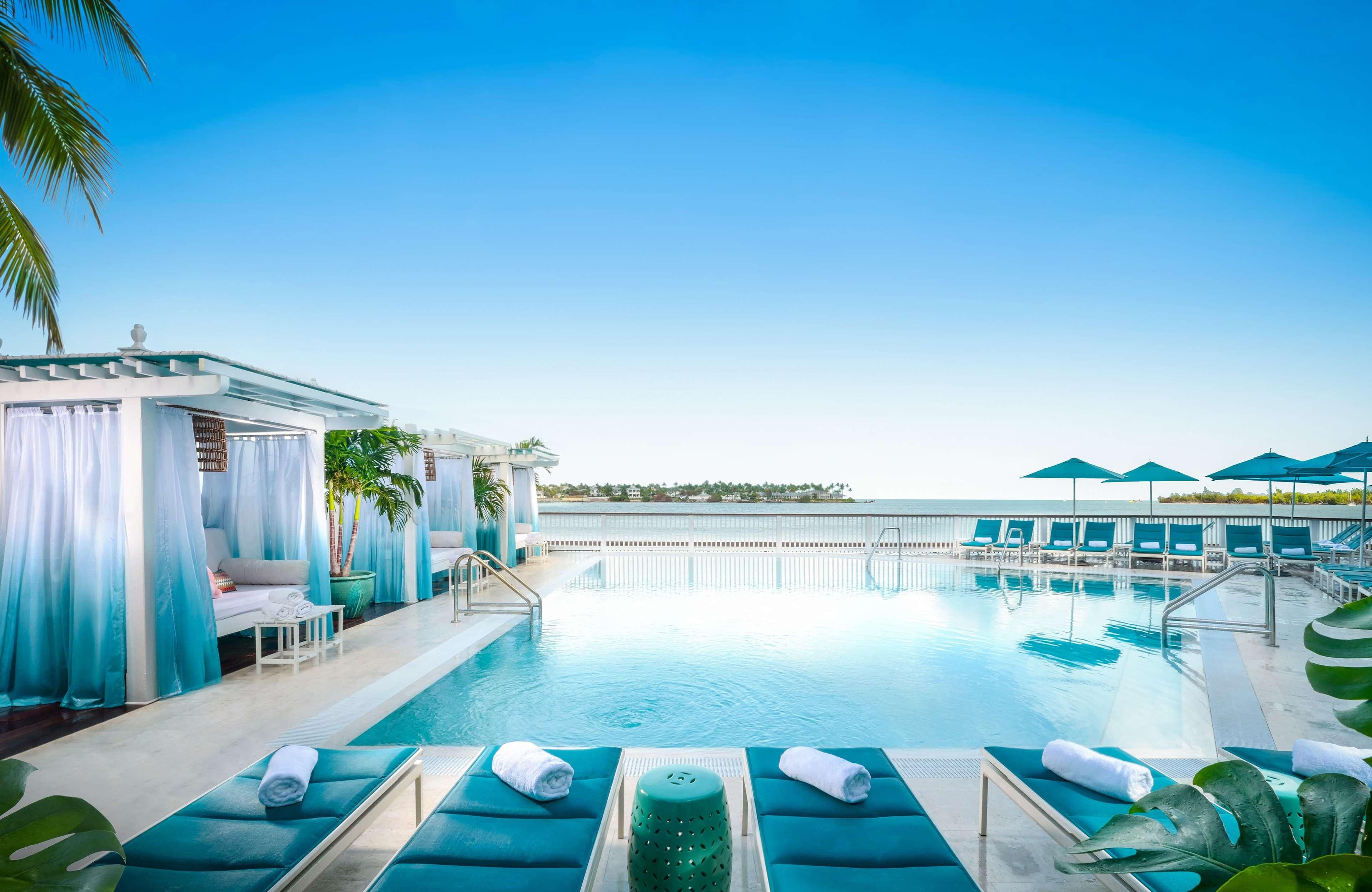 A pool area with lounge chairs, a small seating area, and a view of the ocean.
