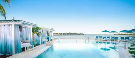 A pool area with lounge chairs, a small seating area, and a view of the ocean.