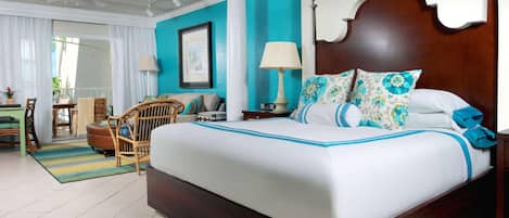 A hotel room with a large bed, a wooden headboard, a white and blue patterned bedspread, a wooden nightstand, a white lamp, and a wicker chair.
