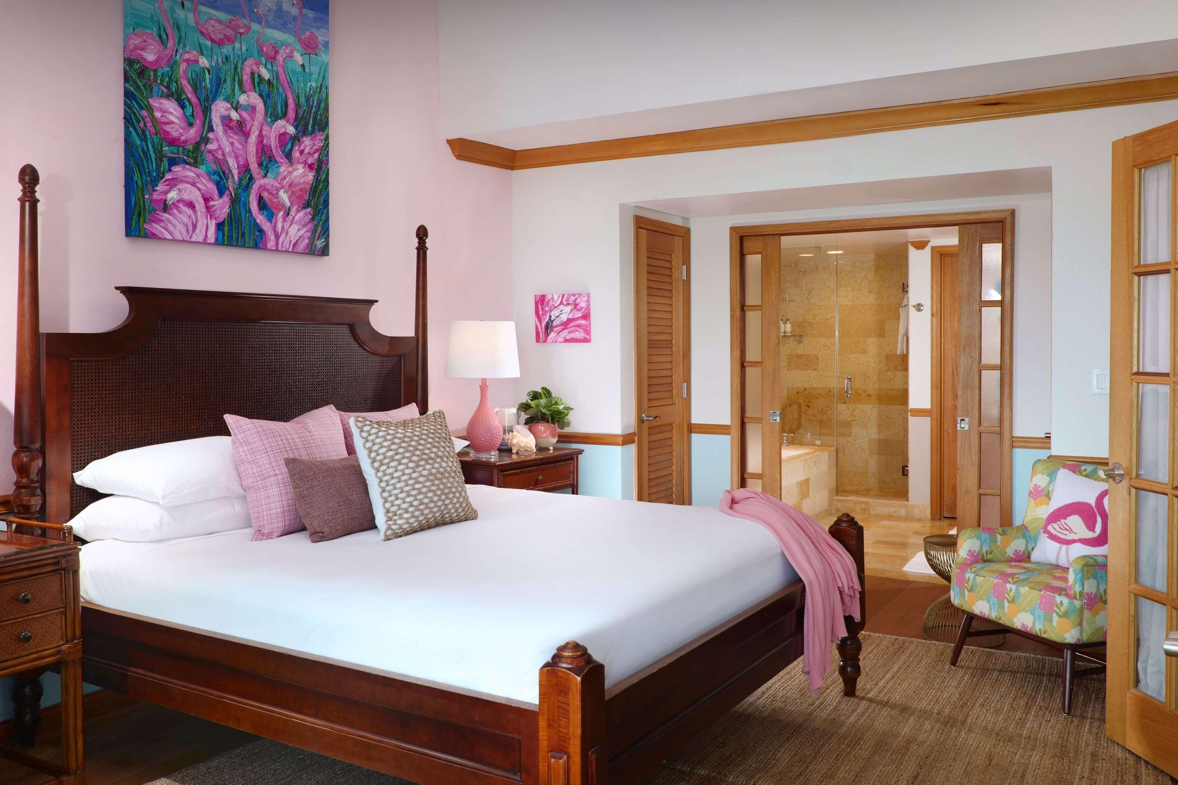 Ein Schlafzimmer mit einem großen Bett, einem Holzkopfstück, Nachttischen, einem Beistelltisch, einem Sessel, einem Gemälde und einem Badezimmer mit Glastür.