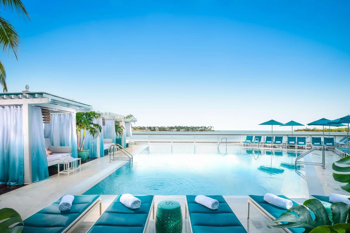 A pool area with lounge chairs, a small seating area, and a view of the ocean.