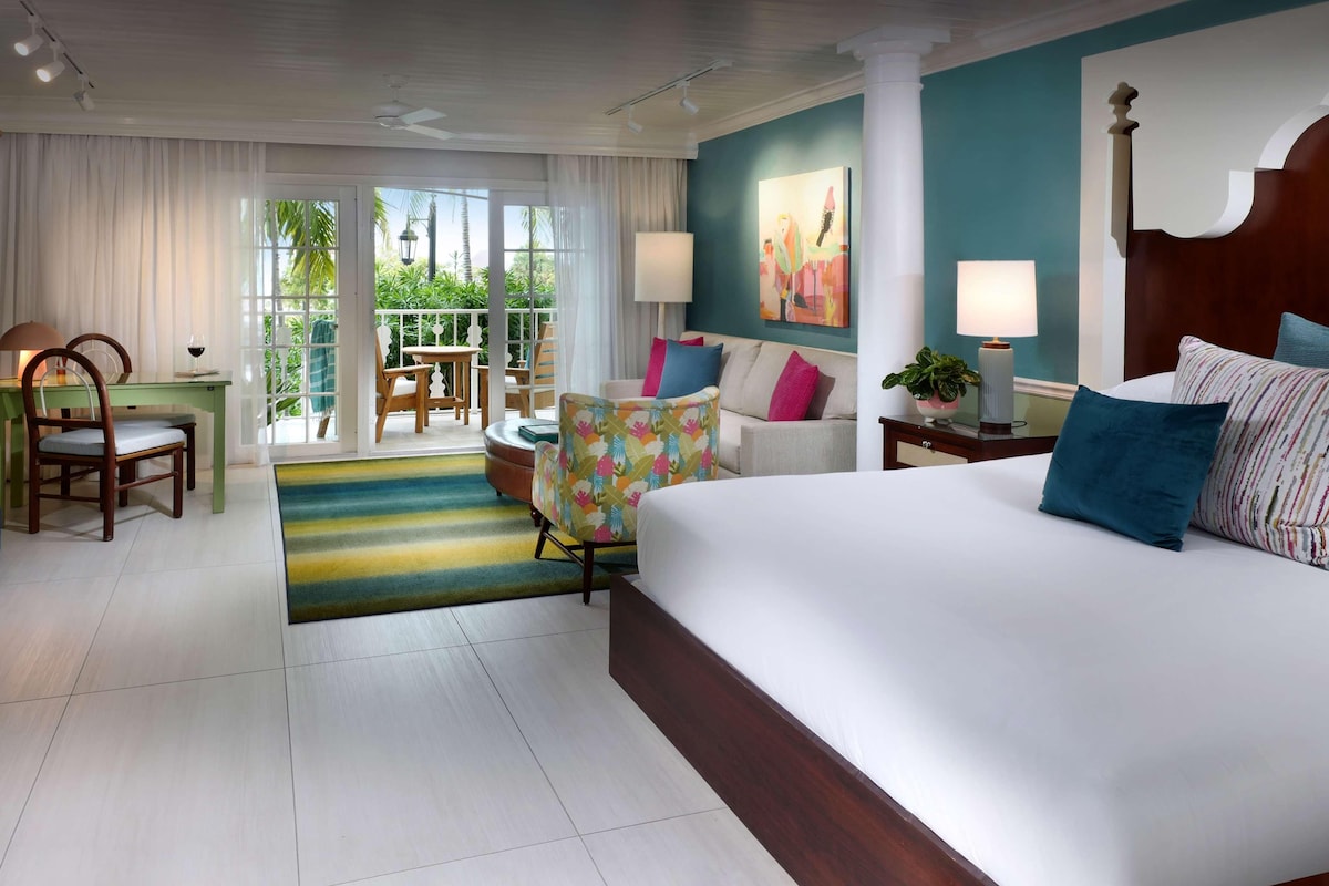 Quarto de hotel com uma cama grande, um sofá, área de refeições com cadeiras, uma mesa e vista para o exterior.