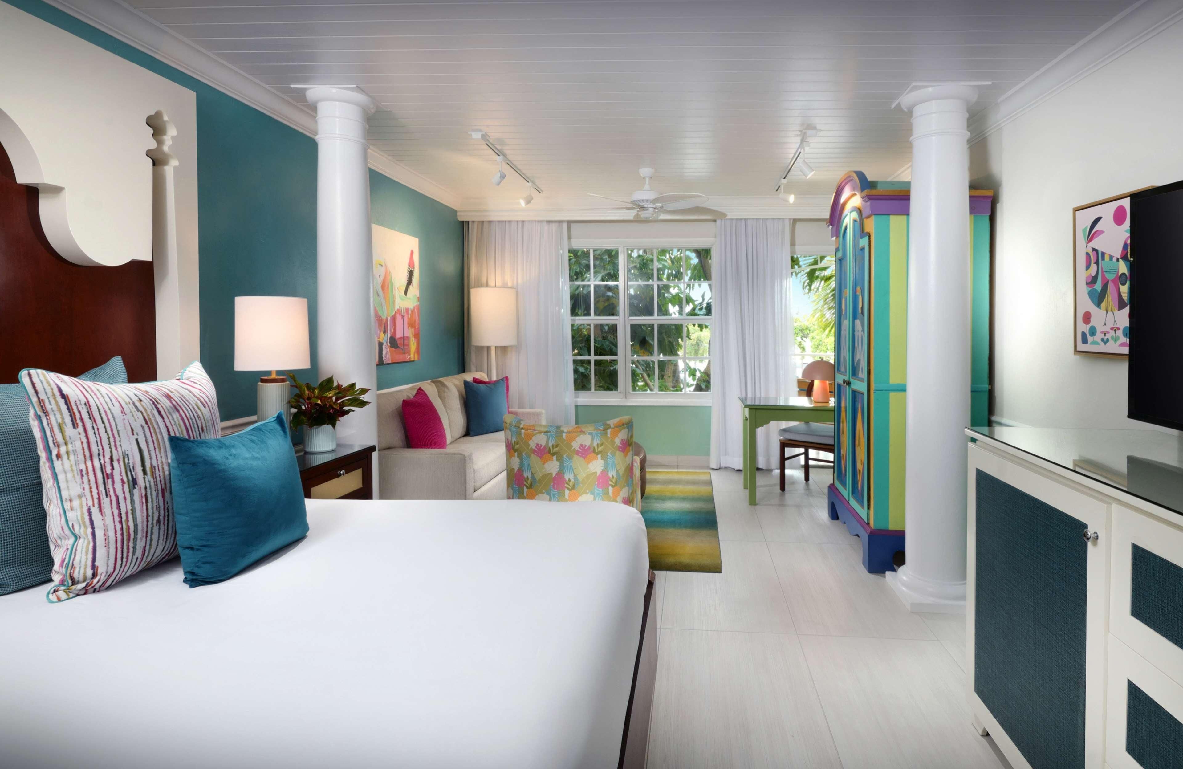 A hotel room with a bed, a desk, a chair, a TV, and a window with curtains.