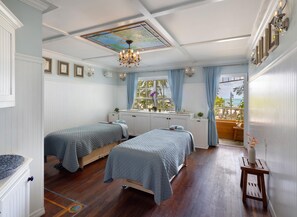 A bedroom with two beds, a window with curtains, a chandelier, and a view of the outdoors.