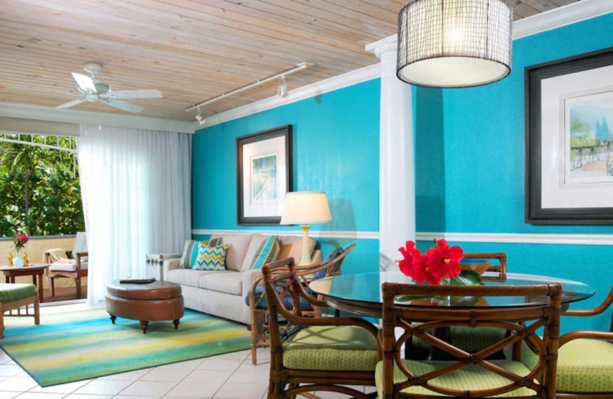 A room with a ceiling fan, a round table with chairs, a sofa, and a large window with curtains.