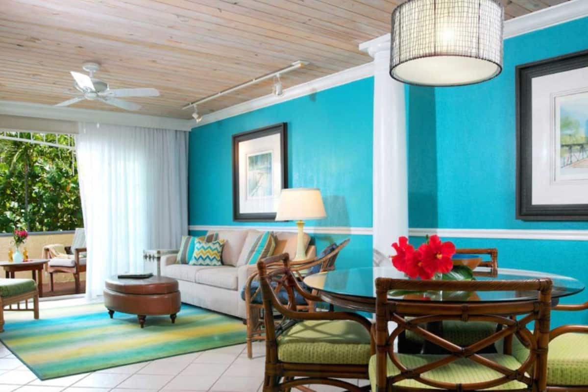 A room with a blue accent wall, a ceiling fan, a round table with chairs, a sofa, and a window with curtains.
