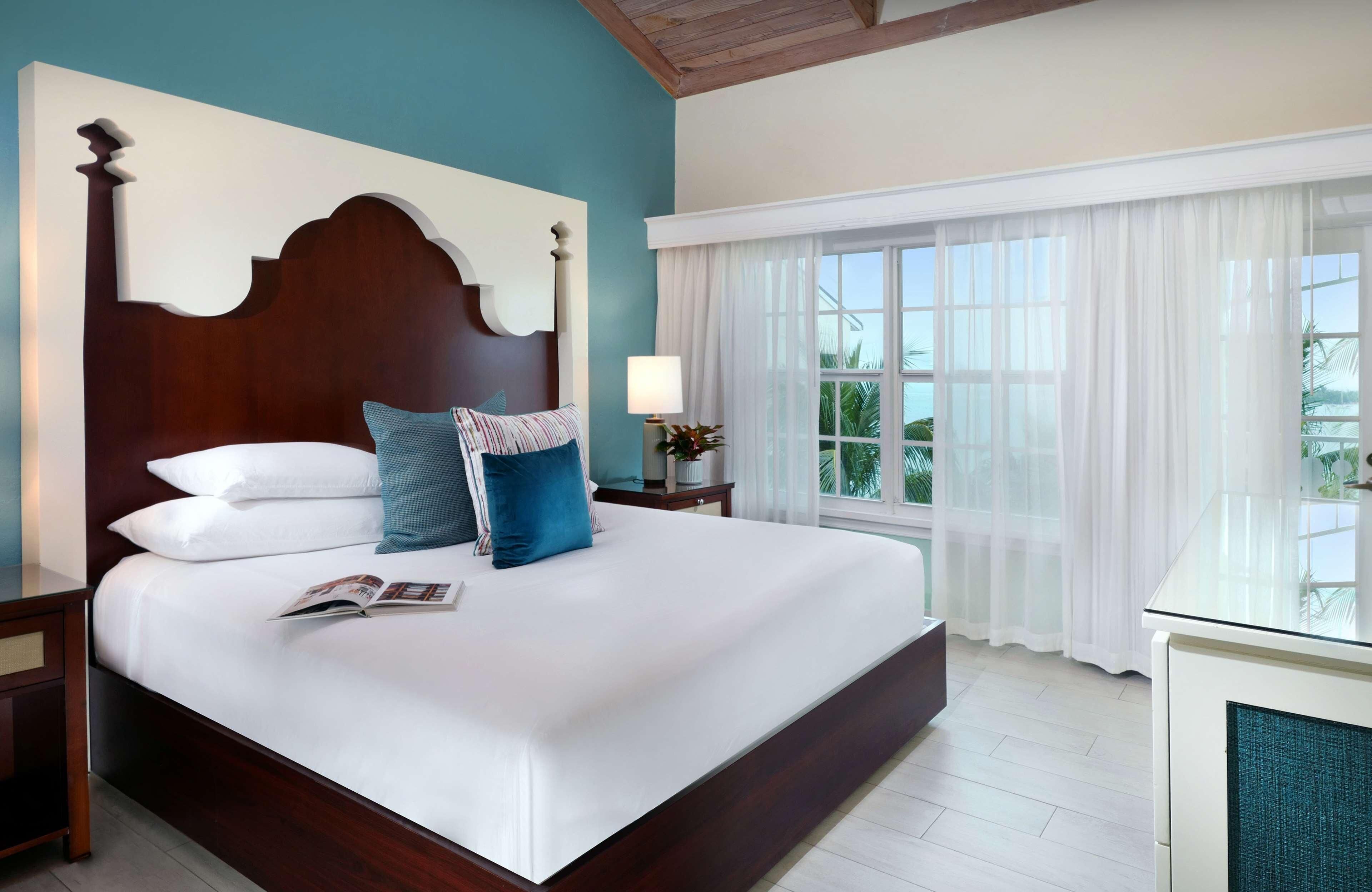 A large bed with a wooden headboard, white bedding, and a single blue pillow.