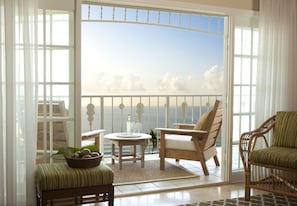 A balcony with a view of the sea, furnished with a chair, a small table, and a bowl of fruit.