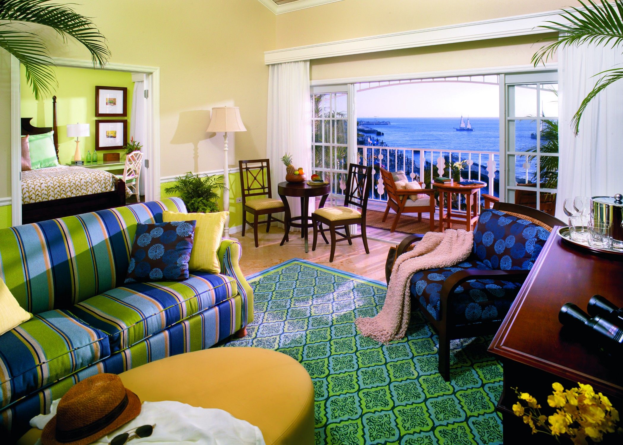 A room with a sofa, chairs, a dining table, and a view of the ocean.