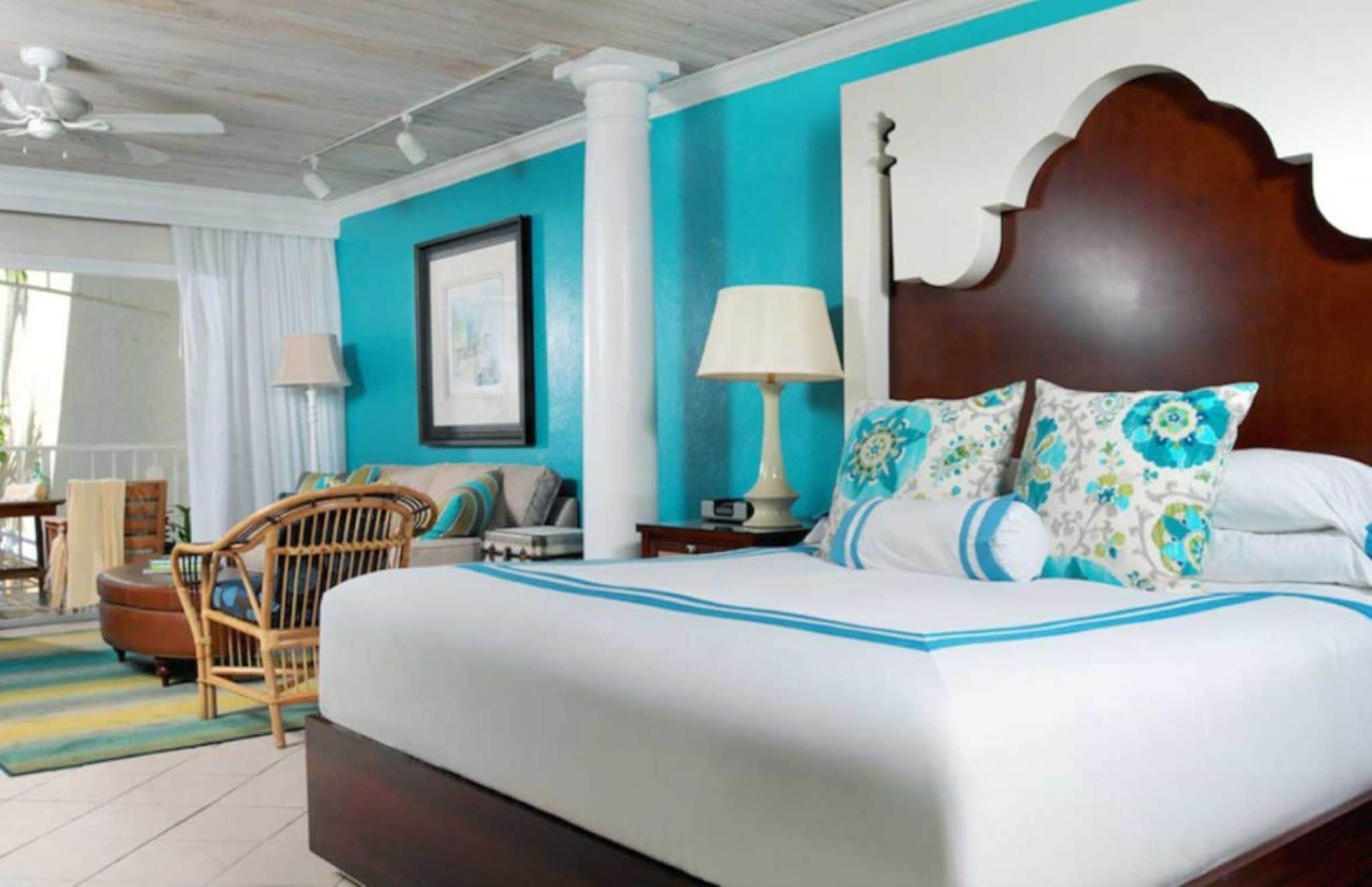 A hotel room with a large bed, a wooden headboard, a nightstand with a lamp, a chair, and a view of the outdoors.