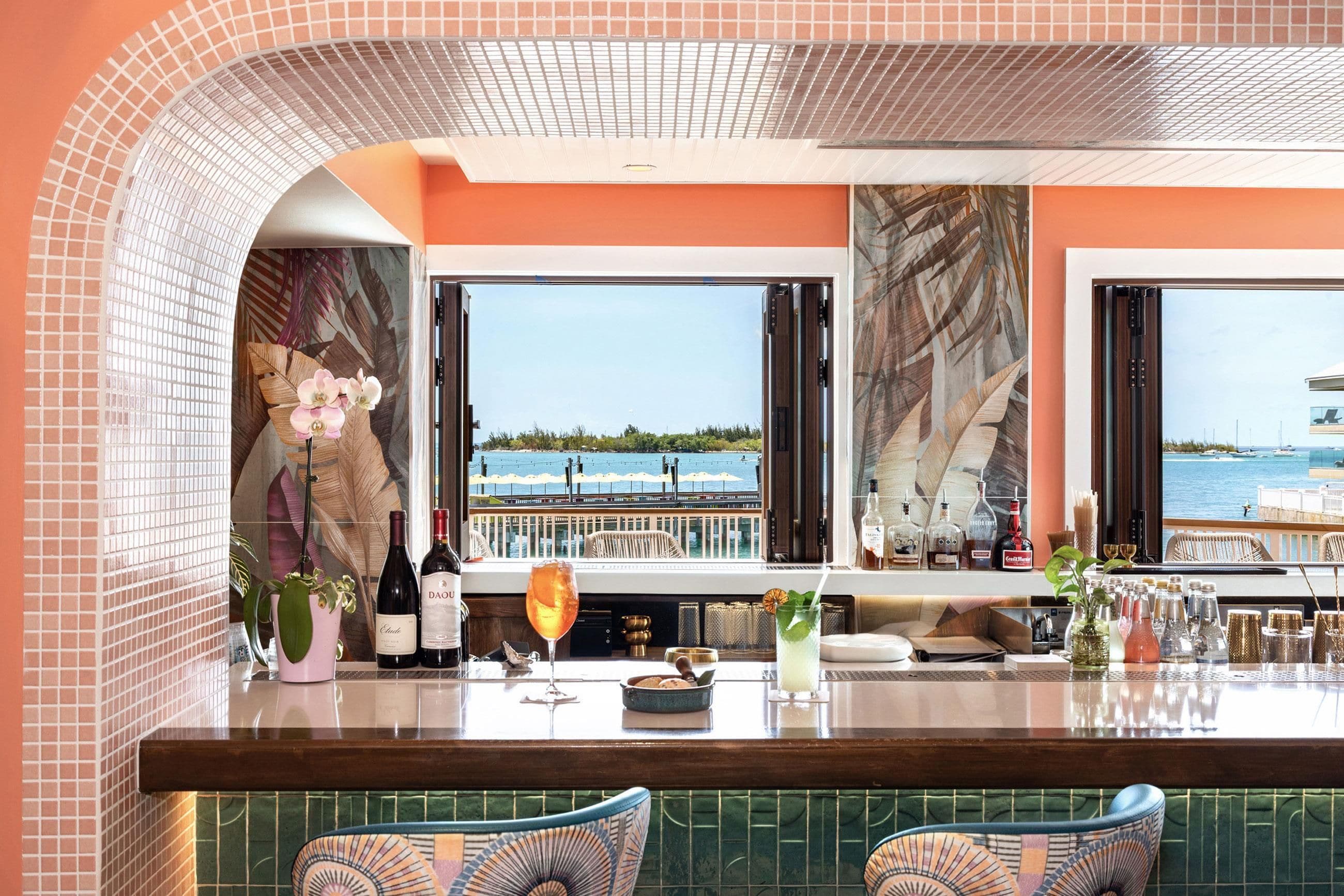 Zona de bar con vista al mar, una botella de vino y una copa de cóctel.