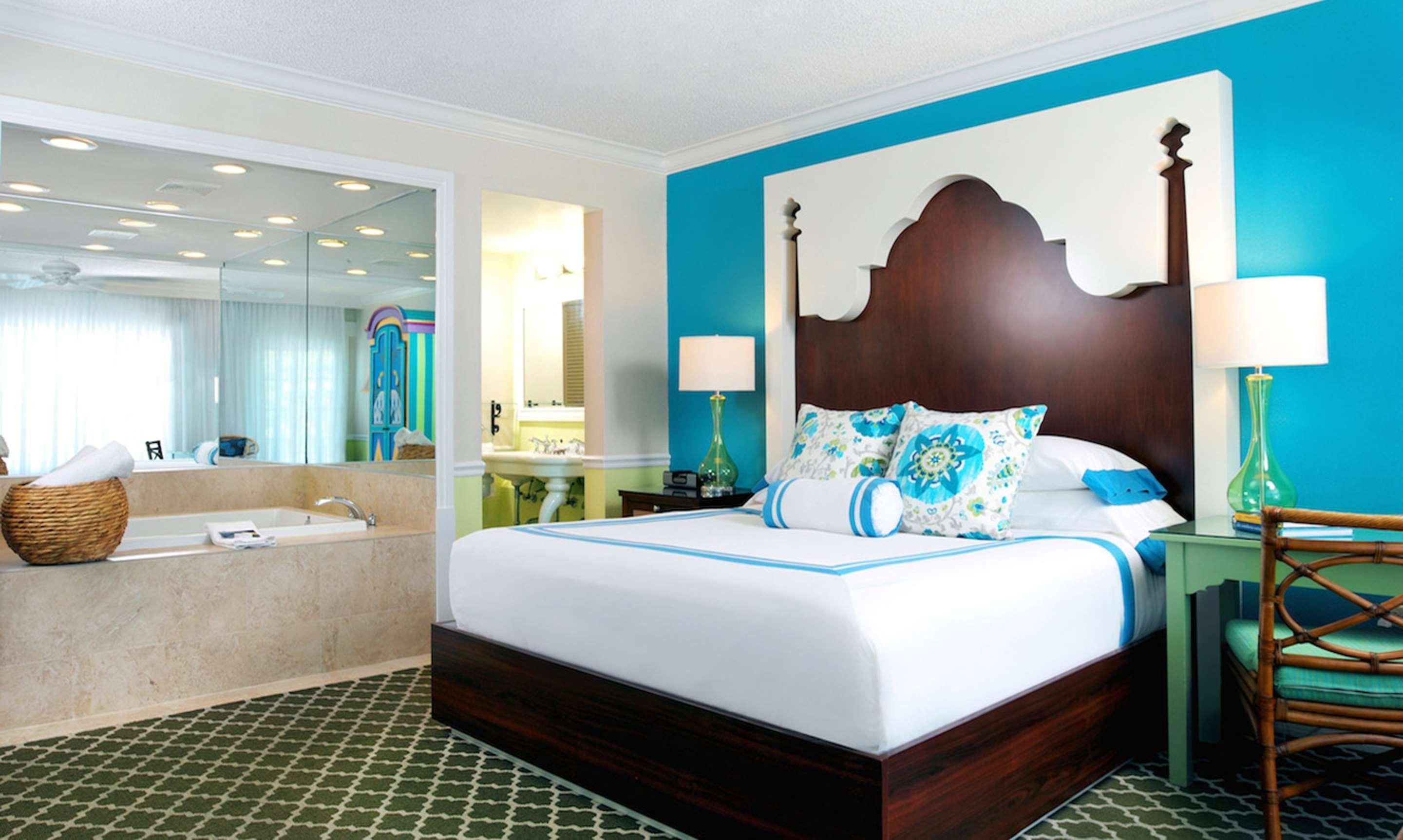 A hotel room with a large bed, a bathroom with a bathtub, and a mirror reflecting the room.