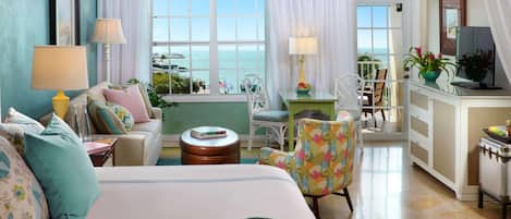 A hotel room with a bed, a sofa, a chair, a small table, a desk, and a view of the ocean.
