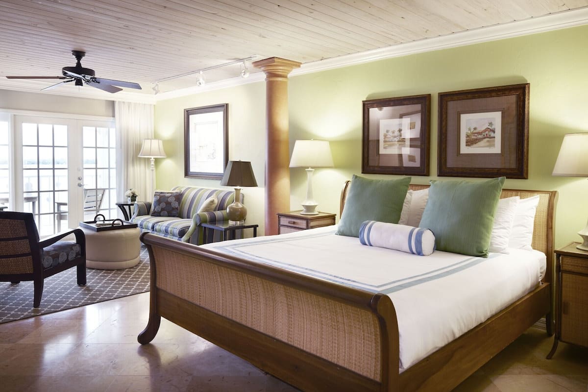 A spacious bedroom with a large bed, a sitting area with a sofa and armchairs, and a view through the glass doors.