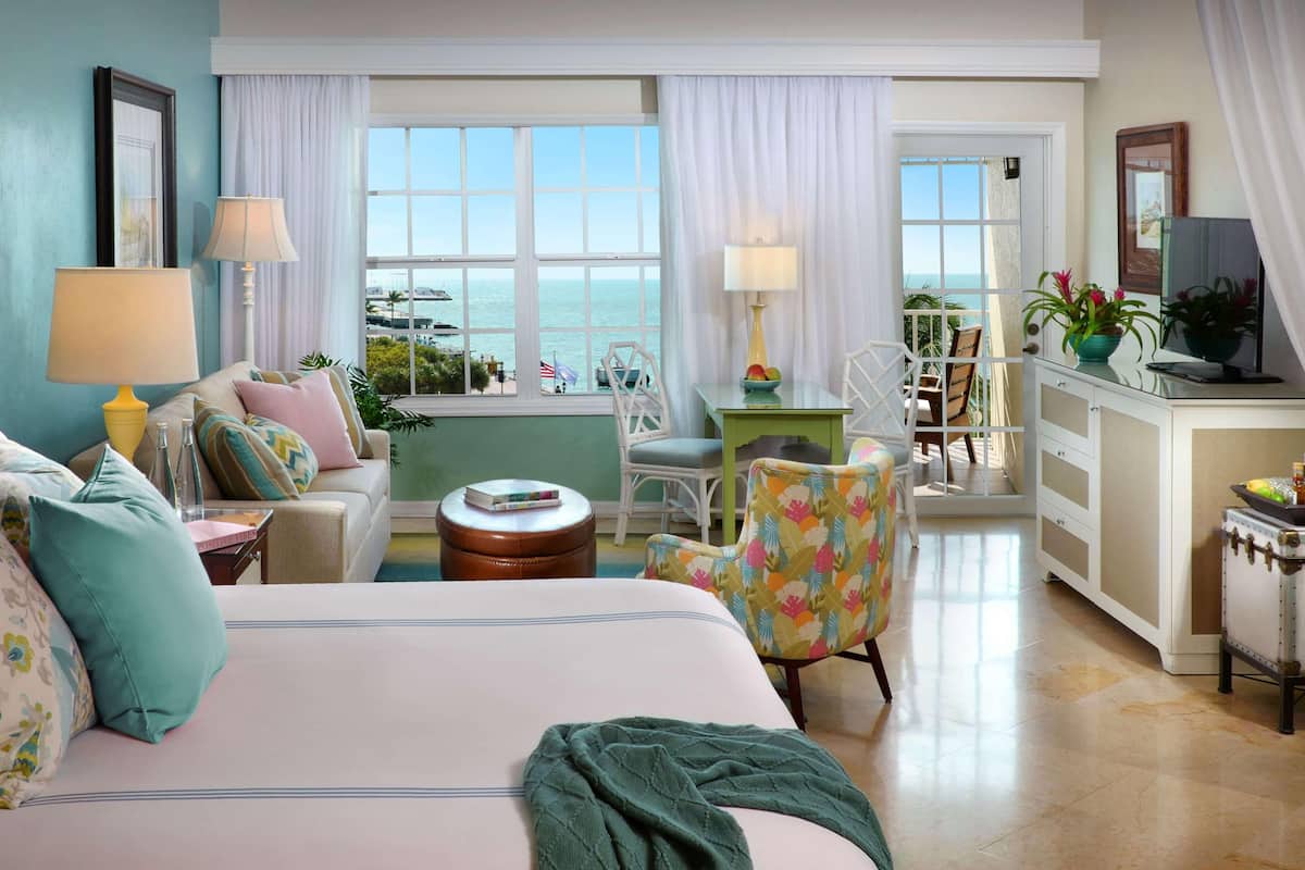A hotel room with a bed, a sofa, a chair, a small table, a desk, and a view of the ocean.