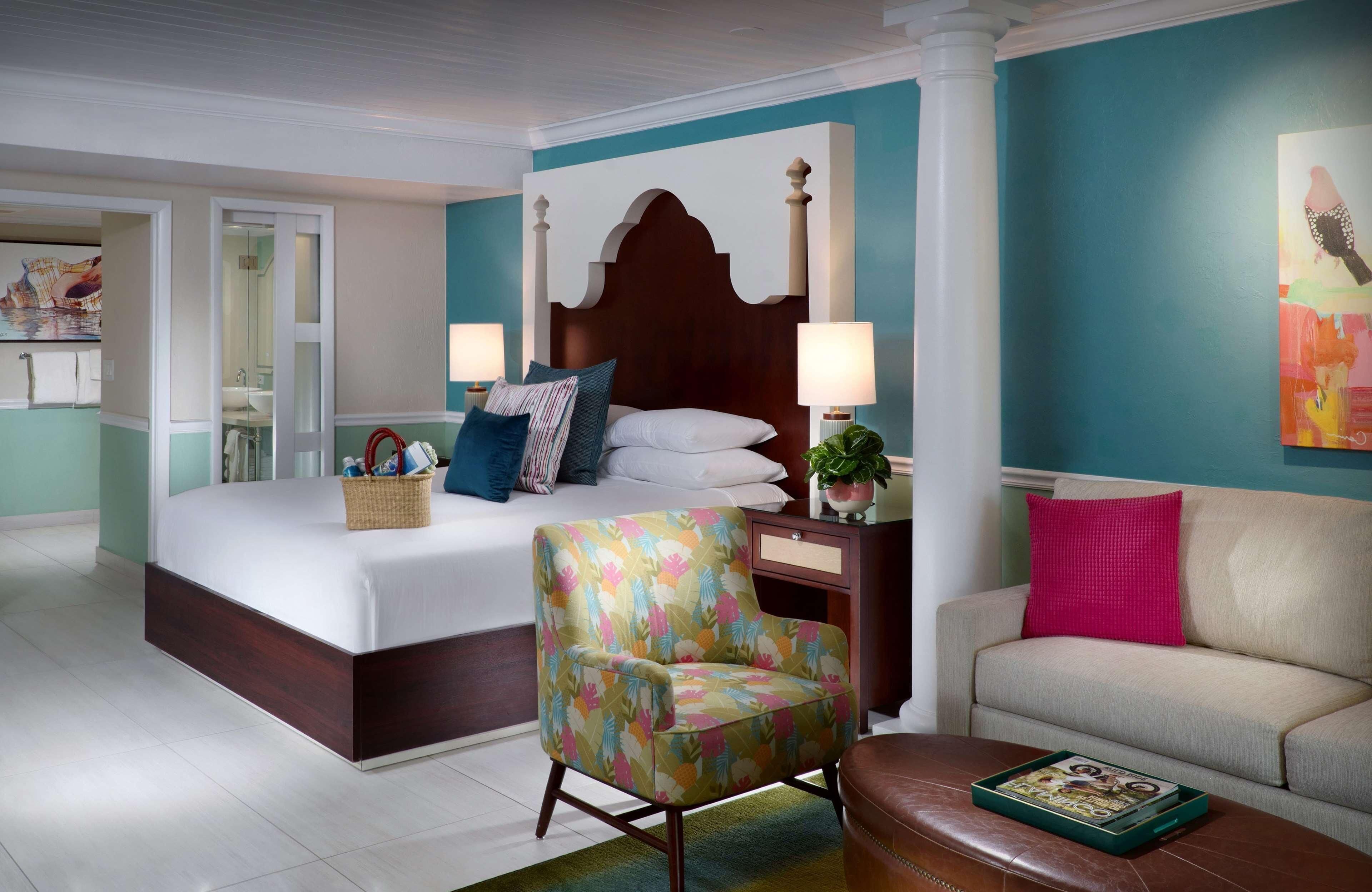 A bedroom with a bed, a chair, a sofa, a nightstand, and a lamp.