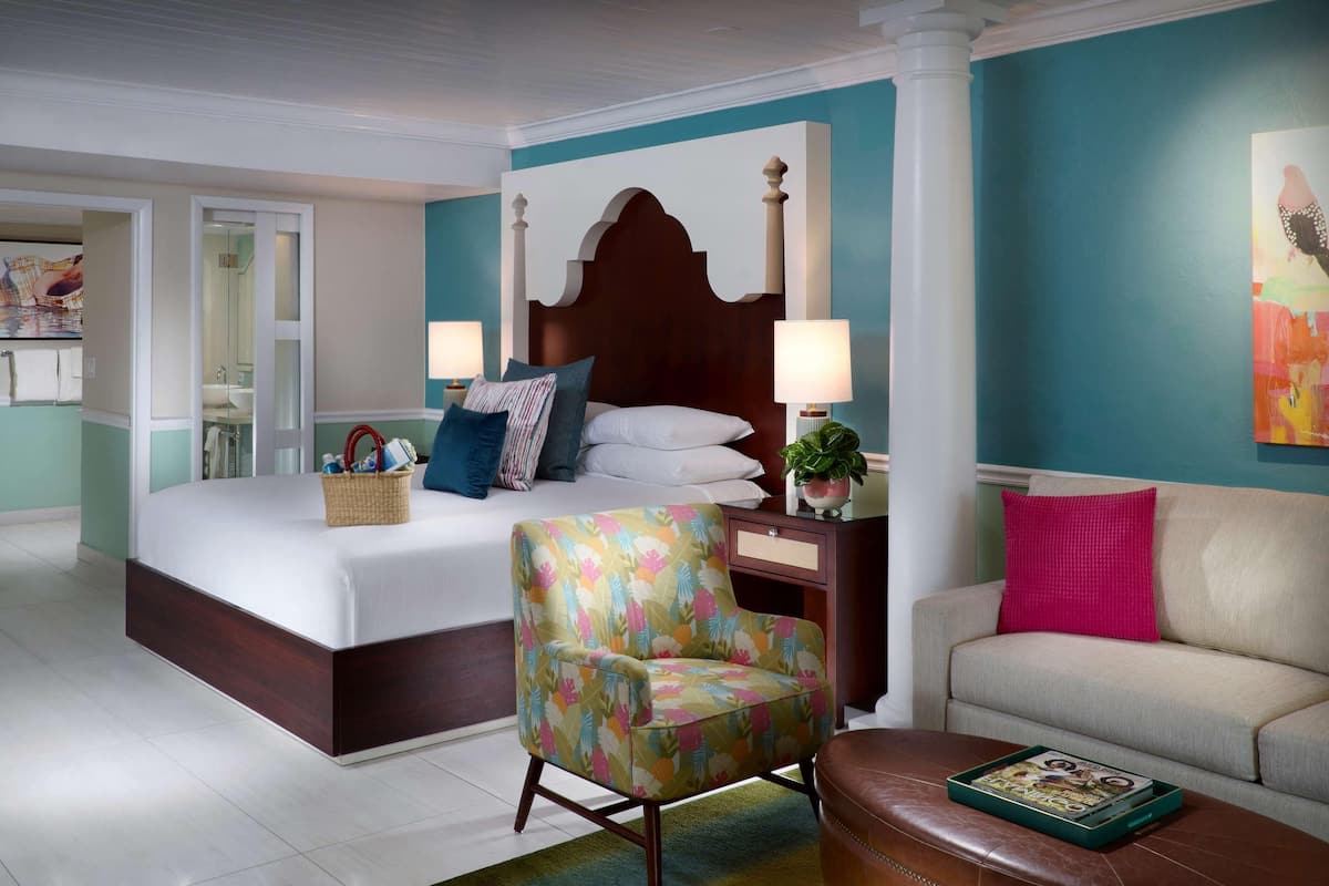 A hotel room with a large bed, a floral armchair, a sofa, and a coffee table.