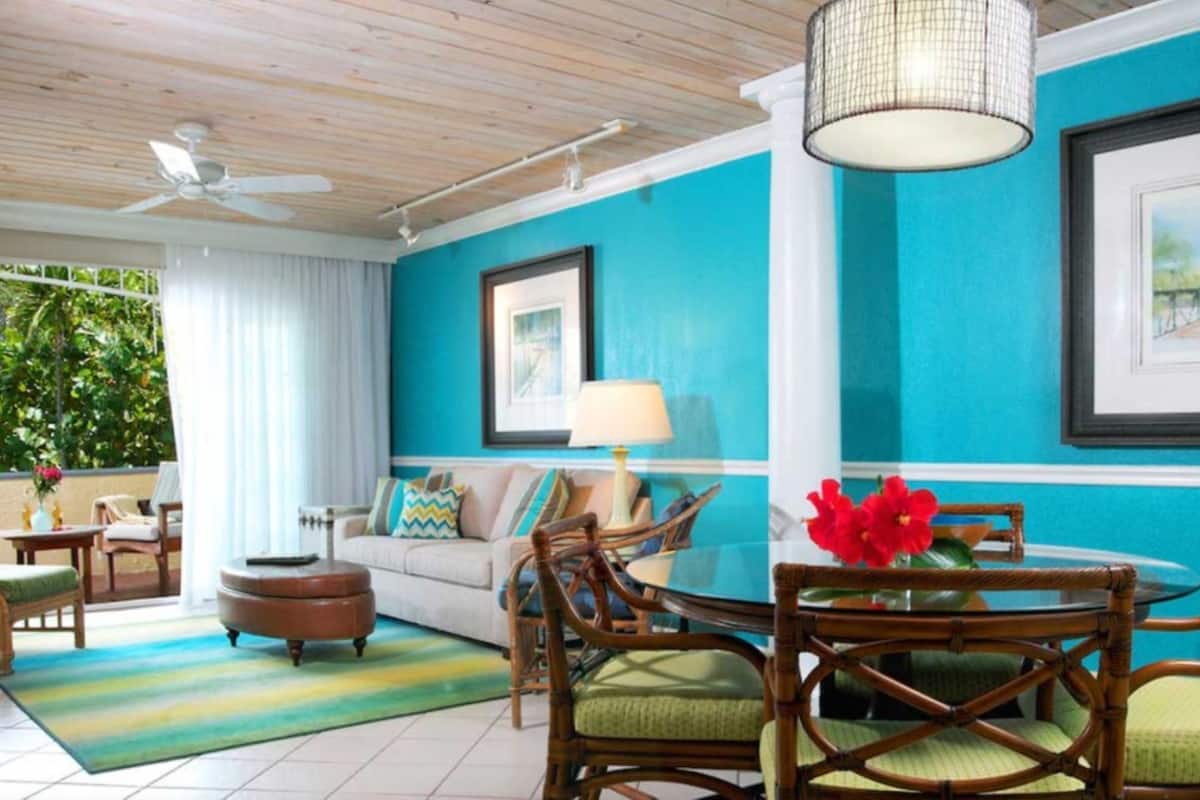 A room with a blue accent wall, a ceiling fan, a round table with chairs, a sofa, and a coffee table.