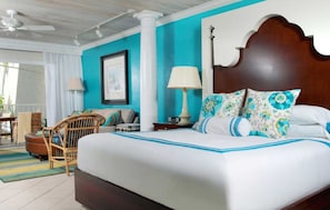 A hotel room with a large bed, a wooden headboard, a nightstand with a lamp, a chair, and a view of the outdoors. - Ocean Key Resort & Spa (Key West)