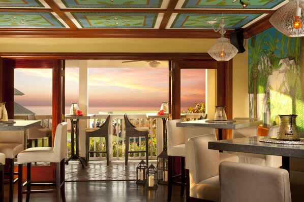 A restaurant with a view of the ocean, featuring a bar area with chairs and tables, and a ceiling with a geometric pattern. - Ocean Key Resort & Spa (Key West)