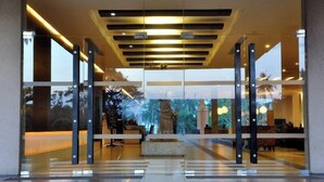 A modern hotel lobby with a reception desk, glass doors, and a ceiling with recessed lighting.