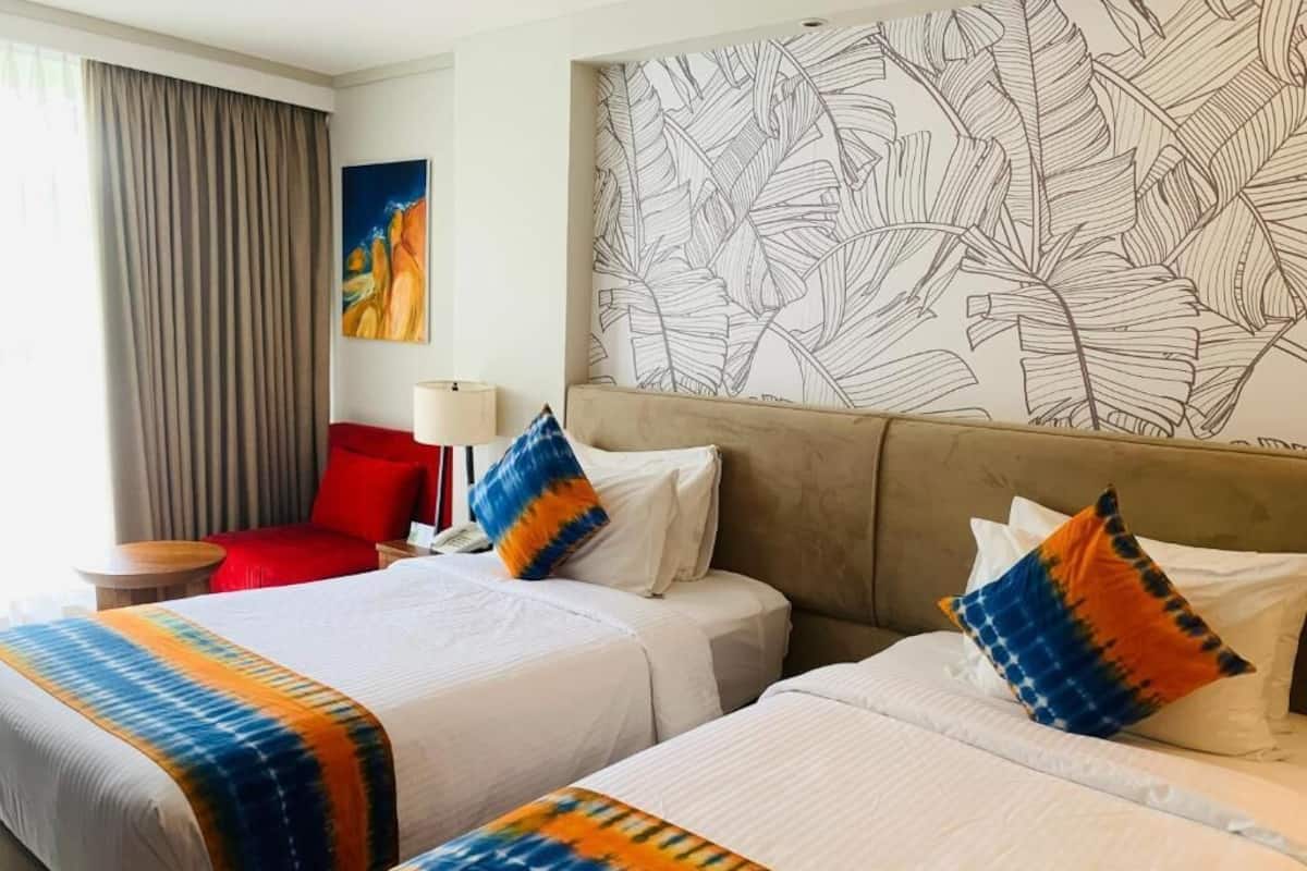 Habitación de hotel con dos camas, una silla roja, una lámpara y un papel tapiz con estampado de hojas.