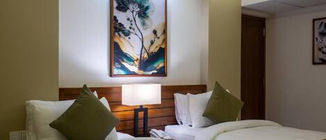 A hotel room with two beds, a nightstand, a lamp, and a painting on the wall.