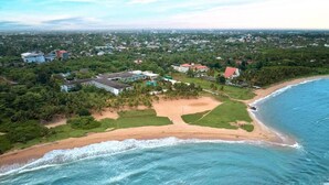 An aerial view of a coastal area with a beach, buildings, and greenery.