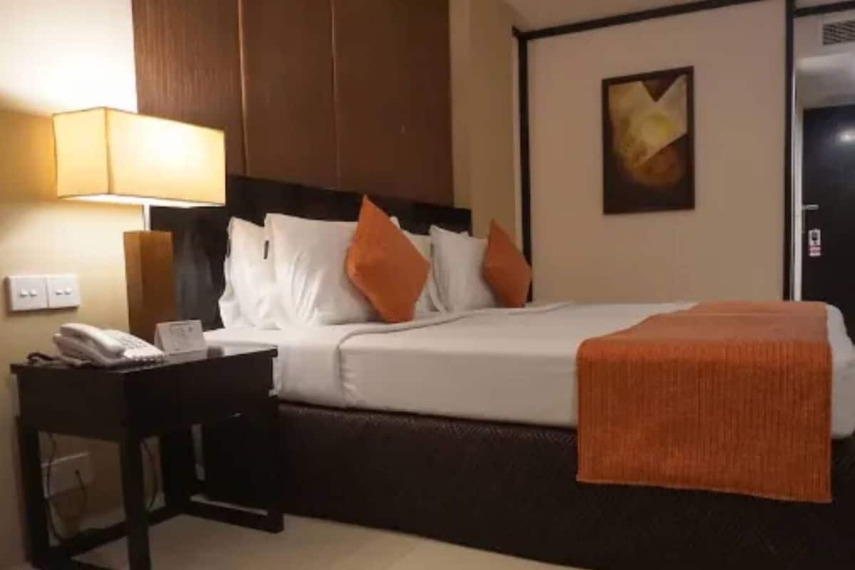 Una habitación de hotel con una cama, una mesita de noche, una lámpara y un cuadro en la pared.