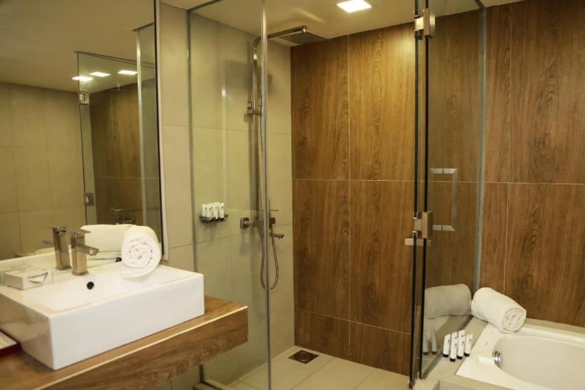 A modern bathroom with a glass-enclosed shower, a wooden vanity, a white sink, and a bathtub.