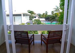 Un balcón con dos sillas de madera, vista a una piscina y follaje circundante.
