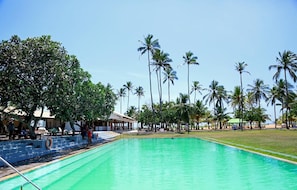 A swimming pool with a clear blue water surface, surrounded by palm trees and a covered seating area. - Pegasus Reef - A Beach Resort in Colombo (Wattala)
