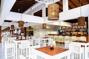 Un restaurante con mobiliario blanco, lámparas colgantes tejidas y una zona de bar.