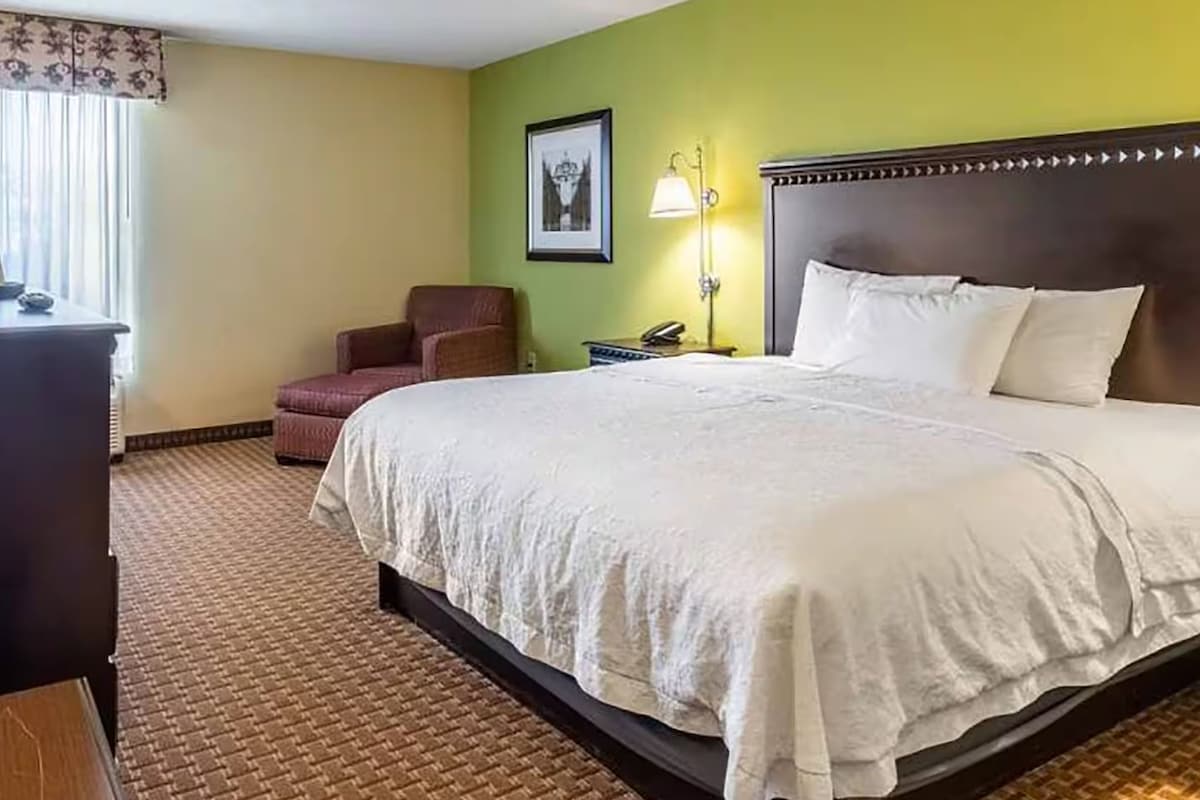 Una habitación de hotel con una cama grande, una silla, un escritorio y una lámpara.