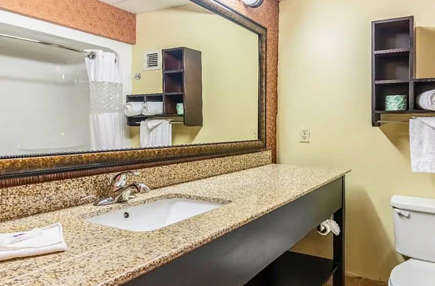 A bathroom with a granite countertop sink, a mirror, a toilet, and a towel rack.