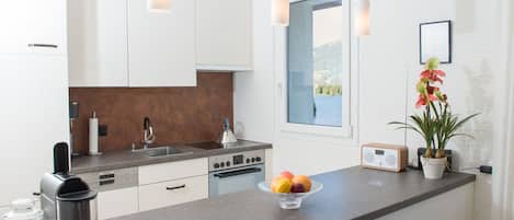 Een moderne keuken met witte kasten, een granieten aanrecht, een koffiezetapparaat, een fruitschaal en een raam met uitzicht op een meer.