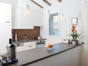 Eine moderne Küche mit weißen Schränken, einer Granit Arbeitsplatte, einer Kaffeemaschine, einer Obstschale und einem Fenster mit Seeblick.