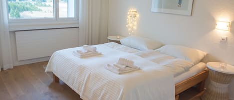 A bedroom with a large bed, two bedside tables, a wall-mounted light, and a window with curtains.