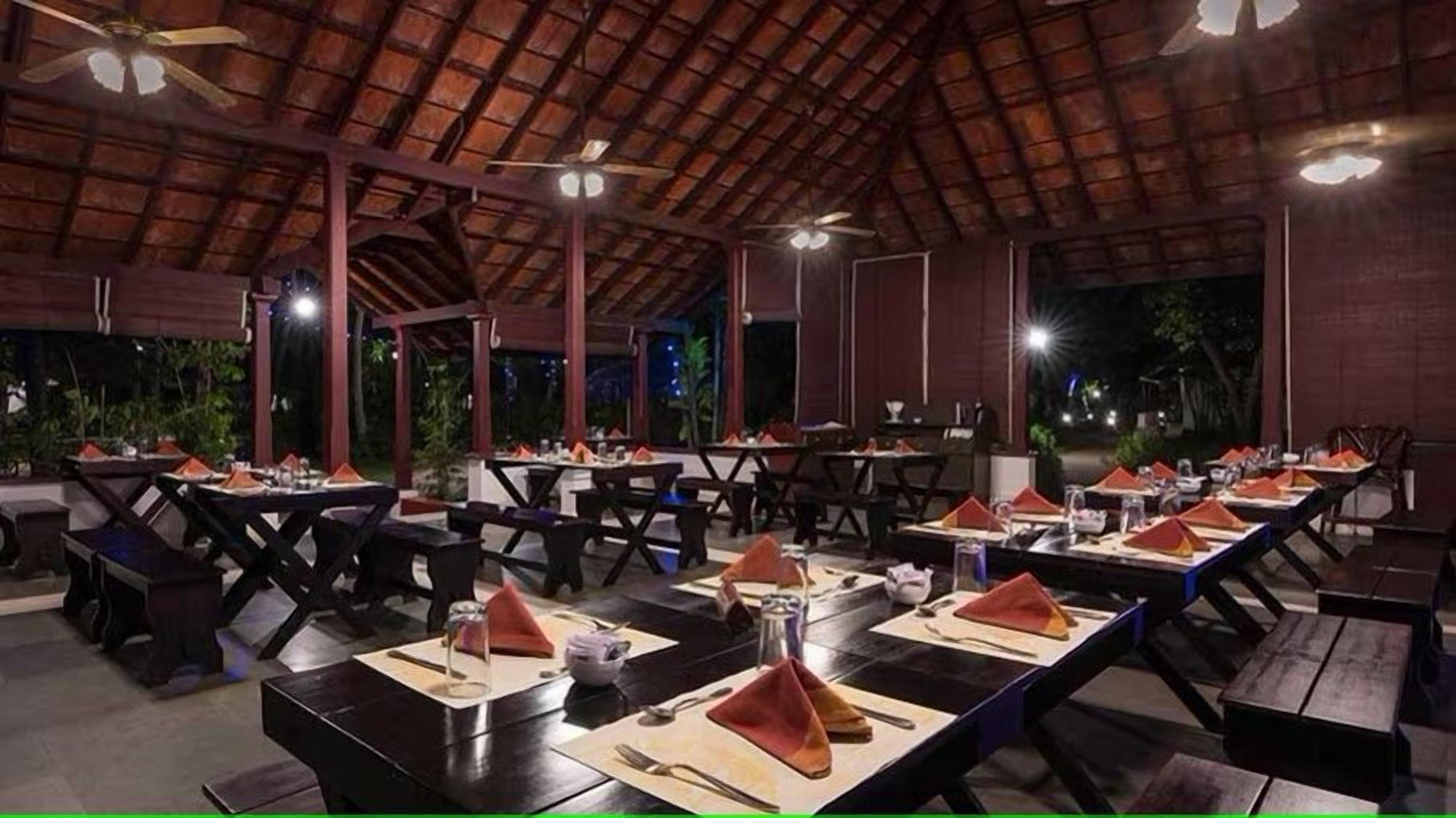 An outdoor restaurant with tables set for dining, a thatched roof, and ceiling fans.