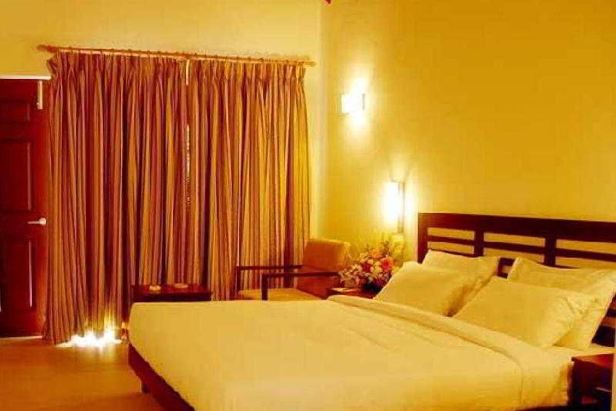 Habitació d'hotel amb un llit, una tauleta de nit, una cadira i una cortina.