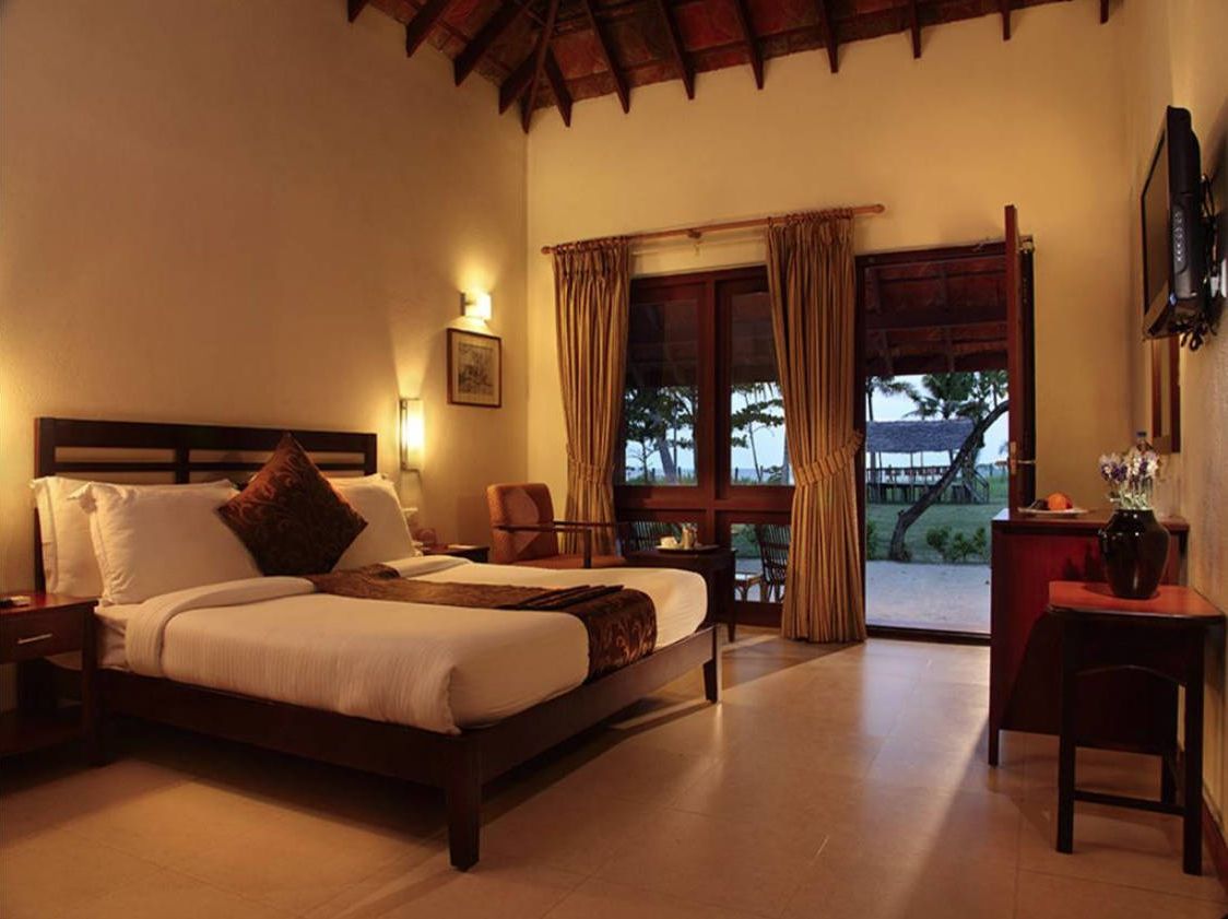 A bedroom with a bed, a desk, a chair, and a balcony with curtains.