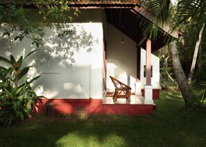 A covered outdoor seating area with a chair, a white building, and surrounding greenery. - Abad Turtle Beach (Ambalapuzha)