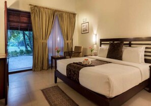 Habitación de hotel con cama, escritorio, silla, ventana con cortinas y vistas a zonas verdes.