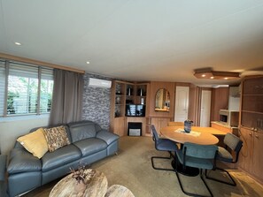 Ein modernes Wohnzimmer mit grauem Sofa, einem Esstisch mit Stühlen, einer Küchenzeile mit Schränken und einem großen Fenster mit Jalousien.