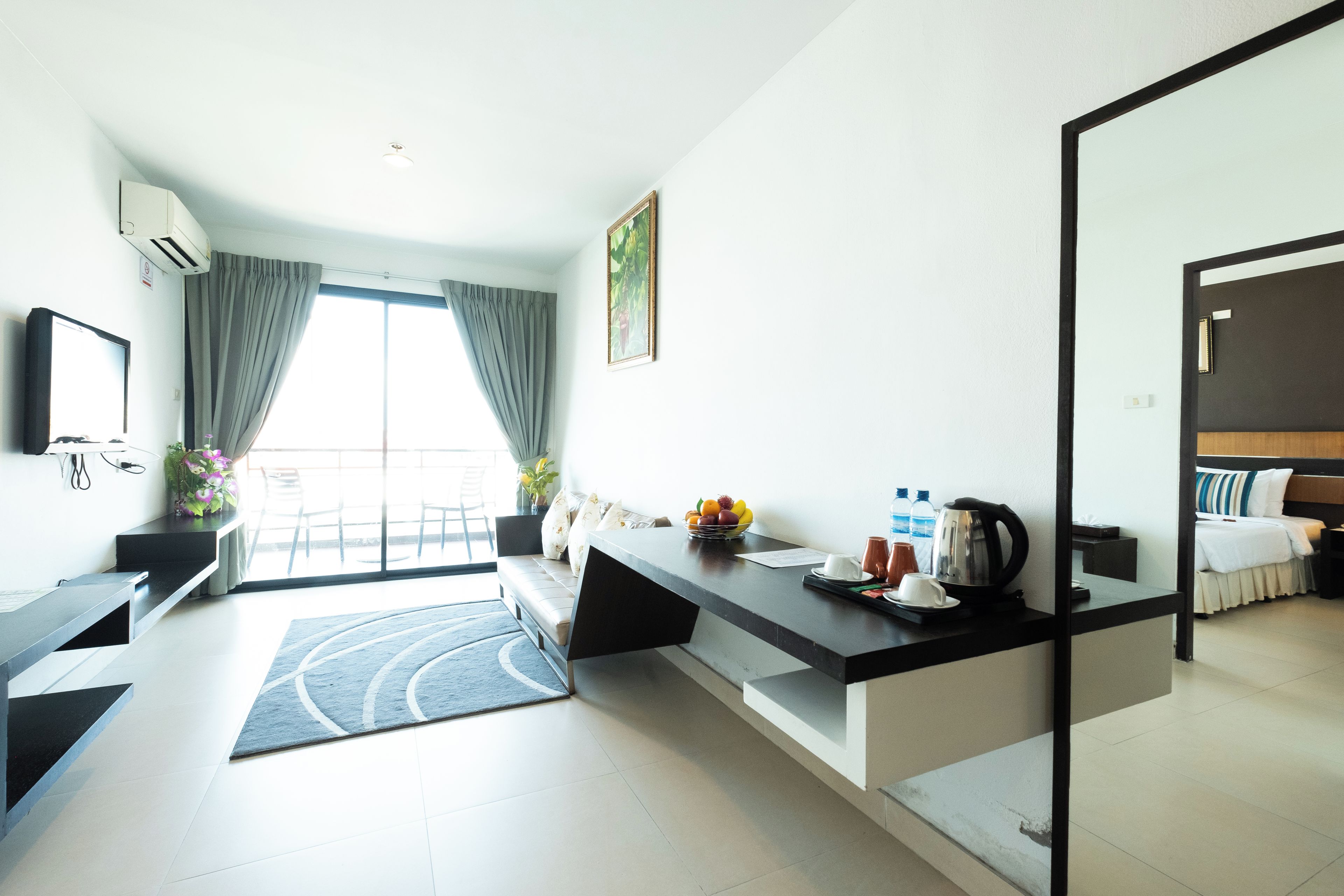 A modern hotel room with a kitchen area, a dining table, and a large window with curtains.