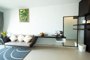 A modern hotel room with a sofa, a small table with a fruit bowl, a mirror, and a trash bin. - The Vogue Hotel, Pattaya (Pattaya)